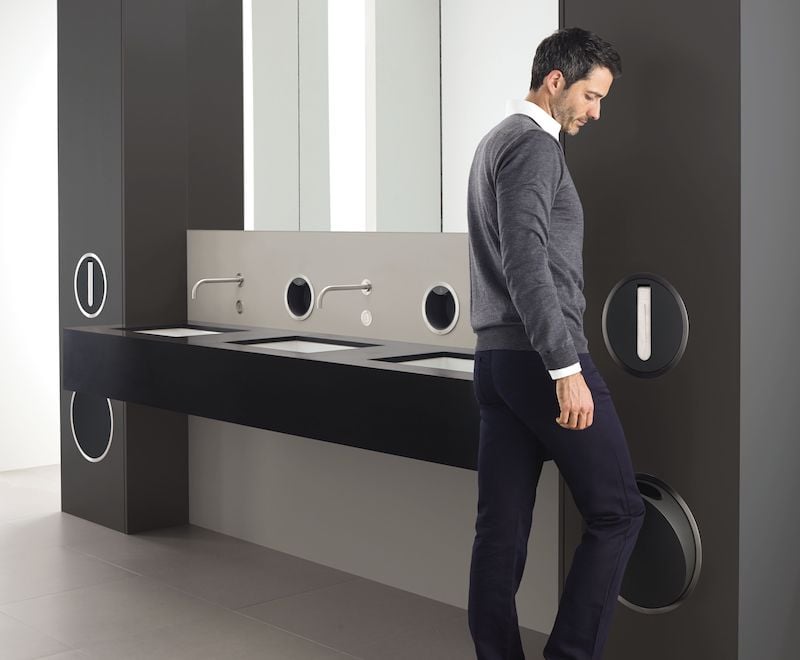 A man standing in a public restroom outfitted with VOLA faucets