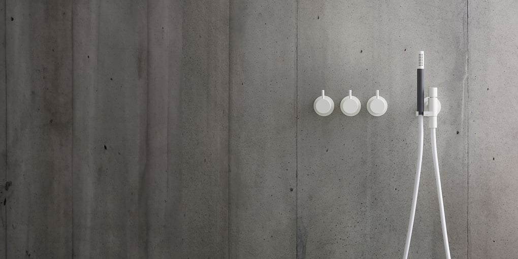 Three shower tap handles and a handheld shower head mounted on a shower wall