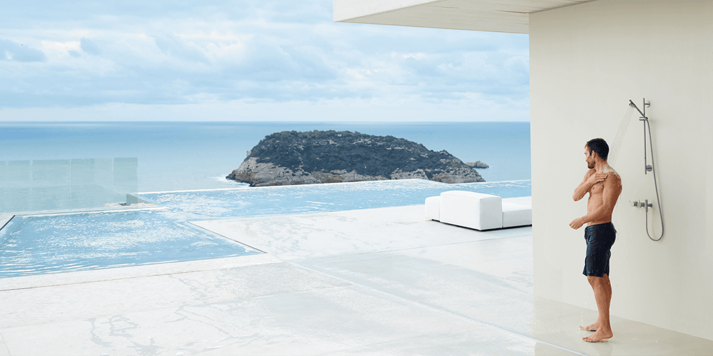 A person showering in an outdoor VOLA shower beside an ocean vista