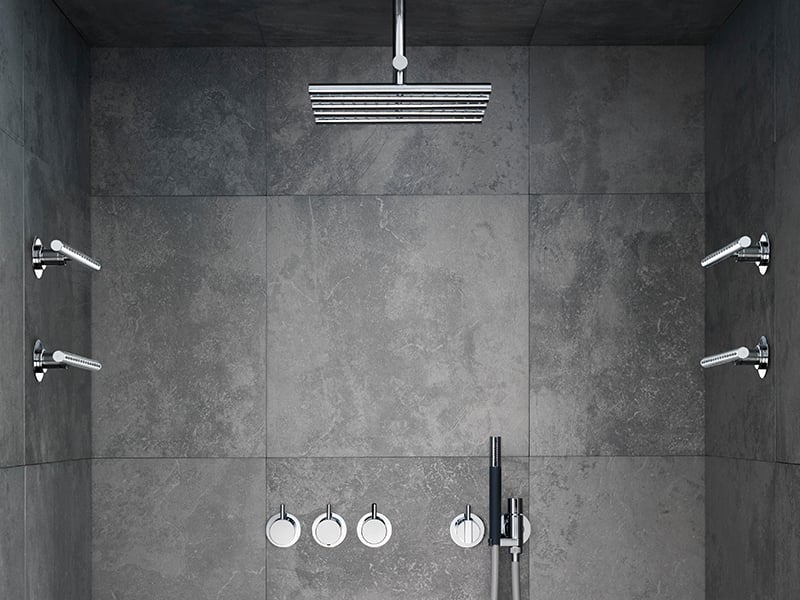 A VOLA shower system with an overhead spray and wall-mounted body sprays