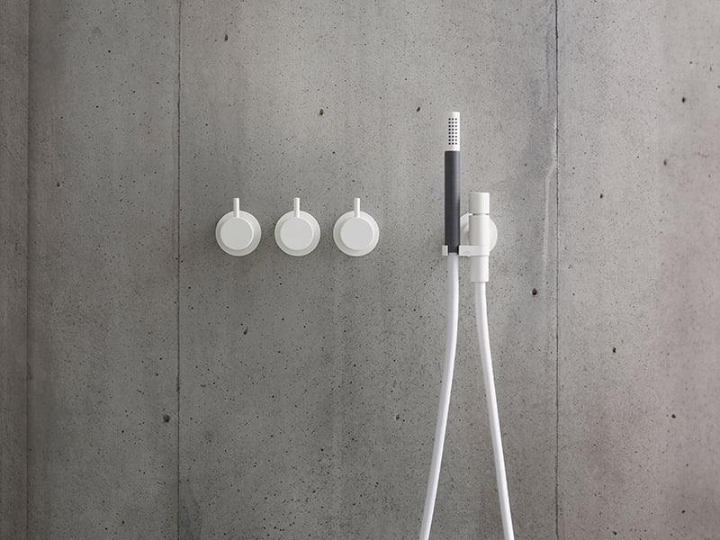 A matte white VOLA shower system mounted on a grey wall