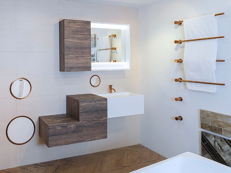 Four bronze towel warmers mounted in a modern wood-look and white bathroom