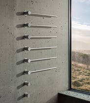Six VOLA towel warmer bars mounted on a gray concrete wall