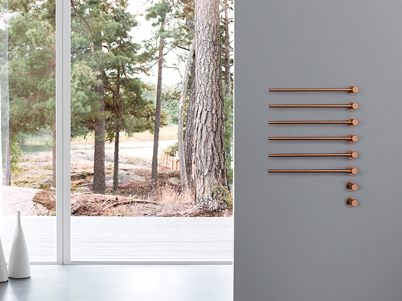 Six copper-colored towel warmers mounted on a grey wall in a bathroom with a forest view